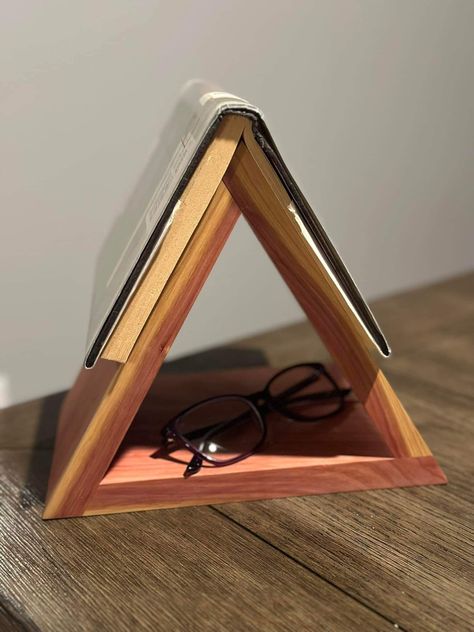 Keep your place and your reading essentials at hand with our Wooden Triangular Book Holder. Expertly crafted from your choice of oak, cedar, walnut, or maple, this elegant and functional piece is perfect for readers who need to step away from their book without losing their place. Its unique triangular design includes a convenient opening in the center to store your reading glasses. Key Features:     Premium Wood Options: Choose from four exquisite wood types--oak, cedar, walnut, or maple. Each offers its own distinctive grain pattern and natural beauty, ensuring your book holder is both stylish and durable.     Handmade Quality: Our book holder is personally handcrafted by me, ensuring superior craftsmanship and attention to detail. The smooth finish and sturdy construction make it a reli Triangle Book Holder Diy, Diy Triangle Book Stand, Wood Book Holder, Wooden Page Holder Pattern, Wood Triangle Book Holder, Reading Essentials, Reading Spot, Booklet Design, Wood Book