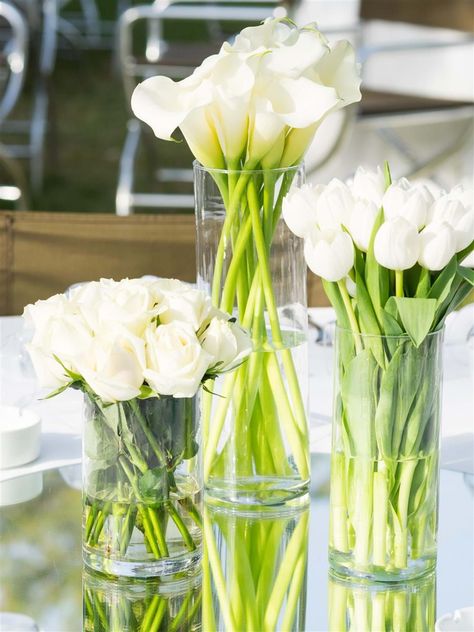 A trilogy of white roses, callas and tulips create a modern and minimalist wedding table decor | Athens Wedding Planner & Designer: @mitheoevents Photo: @JohnNassari Venue: @islandathens | #mitheoevents #weddingplannergreece #destinationweddingplanner #athenswedding #luxurywedding #iranianwedding #athensrivierawedding #weddingstyling #weddingdecor #allwhitewedding #tablesetting #tablescape #tabledecor #weddingflorals #whiteweddingflorals Floral Arrangements For Table, Tulip Centerpieces Wedding, Tulip Wedding Decorations, Tulip Table Decor, Chic White Wedding, Tulip Centerpiece, Wedding Flowers Tulips, Black And White Wedding Theme, White Floral Arrangements