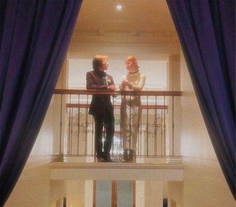 Boy and girl are standing on a suspended walkway with blue curtains on either side. The photo is grainy but the two figures are looking at each other Couple On A Balcony, Balcony Couple Aesthetic, Couple Standing Poses Drawing, Person On Balcony Reference, Balcony Pose Reference, Couple In Balcony, Balcony Couple Photos, Couple Balcony, Irl References