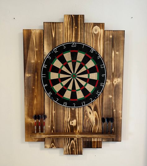 Look forward to an evening of darts with an eye-catcher on the wall. No more arrow holes in the wall with this wooden dartboard. The dimensions when assembled are 70.5 cm x 100 cm x 4.5 cm (w x h x d). Each of our manufactured boards has a unique pattern due to the flambéing (can therefore differ from the product photo). Assembly is guaranteed to be easy thanks to clear instructions and labeling of the individual parts. When you order you will receive: 5 boards in different lengths, 2 smaller sl Dart Board Wood Wall, Homemade Dart Board, Wooden Dart Board Wall, Dart Board Backboard Diy, Darts Setup, Dart Board Wall Ideas, Dartboard Wall, Darts Wall, Hosting Era