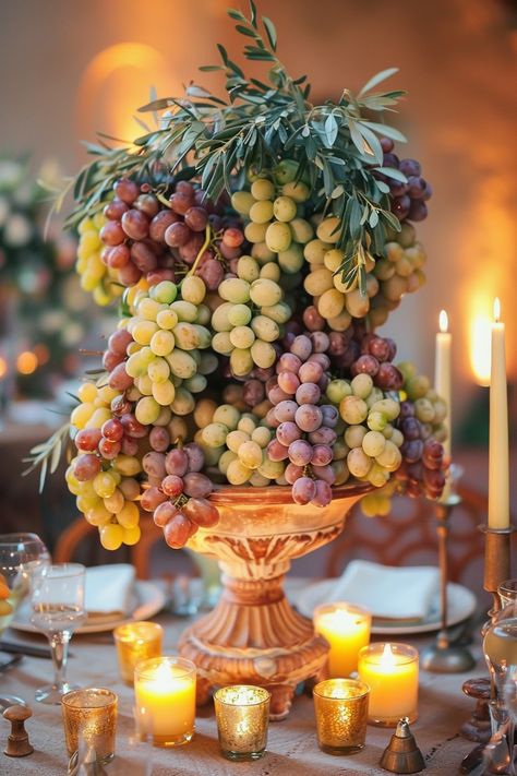 ✨ Elevate your wedding ambiance with a centerpiece that whisks you away to the rolling hills of Tuscany. Experience the charm of Italy as grape vines & olive branches intertwine with the warm glow of candles on your special day. #WeddingInspiration #TuscanWedding #RomanticDecor #WeddingIdeas #CountryChic #RusticElegance #GrapeAndOlive #CandlelightMagic Let the light guide your love story. Tuscany Rehearsal Dinner, Olive Branches Decor, Grape Table Decor, Greek Tablescape, Round Tablescapes Wedding, Grape Wedding Theme, Tuscany Wedding Decor, Roman Feast, Roman Wedding