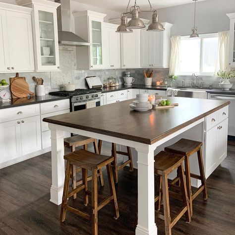 A nickel multi-head pendant light hangs above wooden bar stools arranged under one end of a kitchen island with legs. The white island features a dark stained wood countertop and cabinets with nickel knobs on the other end. Kitchen Island With Chairs, Island With Chairs, Open Kitchen With Breakfast Counter, White Kitchen Island Ideas, Kitchen With Bar Counter, Kitchen Island End Panels, Kitchen Island With Legs, Beadboard Kitchen, Chairs For Kitchen Island