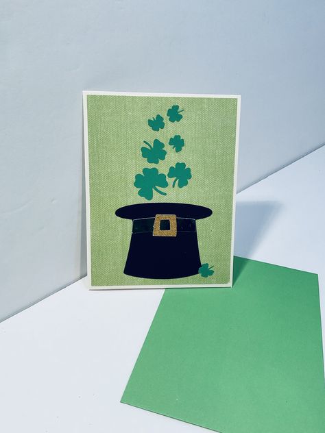 "- standard A2 size (approximately 4-1/4\" x 5-1/2\") card is constructed on a smooth mid-weight ivory cardstock base - the background mat on the card front is a bright green linen textured print paper - featured design element is an upside down black leprechaun hat with green foil hat band and gold non-shed glitter buckle that appears to be releasing several emerald green, variably sized small shamrocks; a small shamrock at the bottom center of the card back carries the theme throughout--all images are die cut - inside sentiment is a traditional Irish blessing: \"For each petal on the shamrock  This brings a wish your way  Good health, good luck and happiness  For today and every day\" which has been printer printed using a non-script font on an ivory paper insert - a green envelope is in Black Leprechaun, Foil Hat, Leprechaun Hat, Leprechaun Hats, Green Envelope, Green Envelopes, Irish Blessing, Irish Traditions, A2 Size