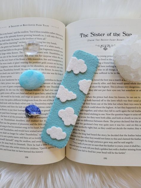 A light blue bookmark with white clouds sitting ontop of a book, surrounded by crystals. Foam Sheet Bookmarks, Gifts With Wool, Book Marks Felt, Felt Bookmarks Handmade, Bookmark Clouds, Kids Bookmark Craft, Small Felt Projects, Diy Felt Bookmarks, Bookmark Handmade Ideas