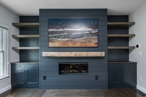 🔥Why not create a stunning focal point in your home with a new fireplace design? This living room is a cozy space with dark blue paneling and cabinets surrounding the fireplace, accented by a rustic wood mantel and shelves.  ☎️Call us at (781) 871-0881 to create your ideal fireplace design! Dark Blue Panelling, Dark Blue Fireplace, Blue Paneling, Blue Fireplace, Wood Mantel, Wood Mantels, The Fireplace, Updating House, Living Room With Fireplace