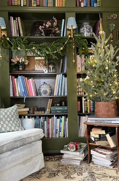 English Cottage Bookcase, Wreaths On Bookshelves, Olive Green Library, Sofa In Front Of Bookcase, Colored Bookshelves, Bookcase Christmas Decor, Christmas Bookcase Decor, Green Library Room, Eclectic Bookshelf