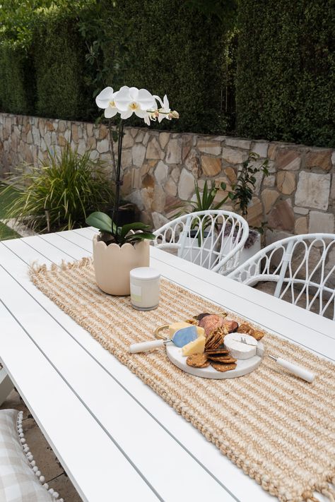 Create your own outdoor Hamptons space with our 5 easy tips. Hamptons design style is an increasingly popular style. With this stunning white outdoor dining table, subtle striped jute table runner, white orchid, white wicker chair, white orchid, and of course this gorgeous round cheese board. For more ideas to help you achieve a Hamptons look, click on the pin or go to StyleCurator.com.au. White Outdoor Dining Tables, White Metal Outdoor Table, Outdoor Dining Styling, Hamptons Outdoor Dining, White Outdoor Dining Chairs, Outdoor Dining Table Styling, White Outdoor Dining Set, Outdoor Entertaining Area Australian, Outdoor Table Styling