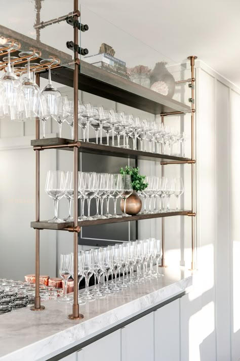 Amuneal's Collector's Series is used as bar shelving at Earl's Beach House Restaurant. This unit mounts to the bar and ceiling, providing a stable and luxurious display for glassware. #barshelving #barideas #shelving Gold Bar Shelving, Over Bar Shelving, Metal And Glass Shelves, Bar Glass Display Ideas, Commercial Bar Glassware Storage, Restaurant Bar Shelves, Bar Organization Ideas Restaurant, Bar Glasses Display, Hanging Bar Shelves