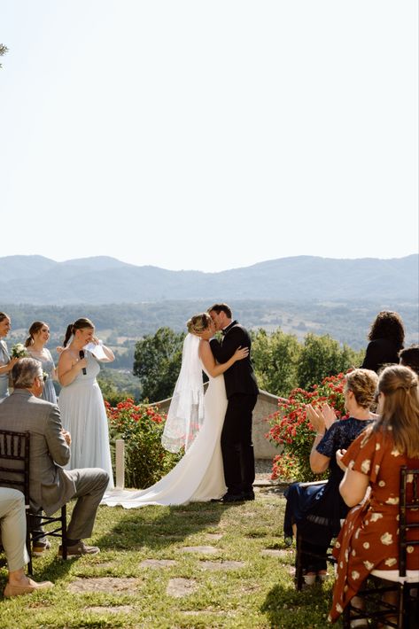 bride and groom stand in front of their friends and family and share their first kiss. In the background are mountains and the tuscan countryside. Wedding First Kiss Pose, First Kiss Pose Wedding, Wedding Ceremony Kiss Pose, Wedding First Kiss Photo, Wedding First Kiss Photography, Ceremony First Kiss, Wedding Ceremony Kiss, Wedding First Kiss, Ceremony Kiss