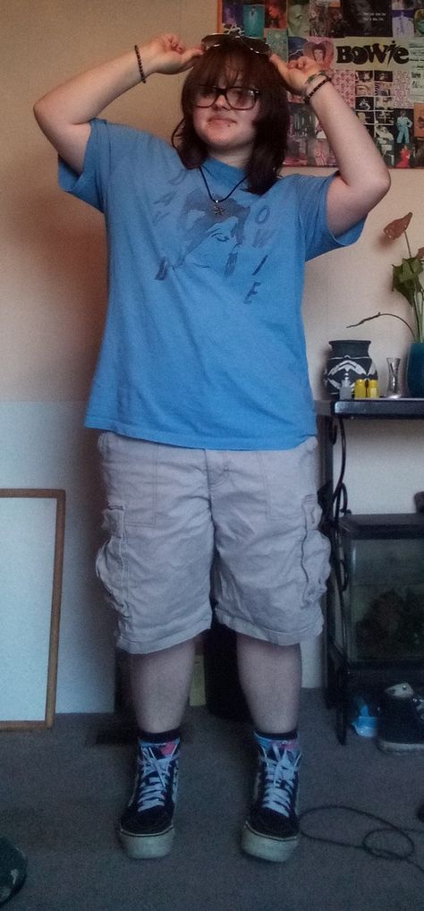 a summer outfit on a teen with shaggy shoulder length brown hair.the outfit consists of a light blue shirt with David Bowie's face and the words "David Bowie, khaki shorts, blue Patrick socks, original vans, and sunglasses on the teens head. Transmasc Outfits Plus Size, Plus Size Transmasc Fashion, Trans Summer Outfits, Trans Masc Outfits Plus Size, Summer Trans Masc Outfits, Chubby Masc Outfits, Masc Plus Size Outfits, Trans Masc Clothes, Trans Masc Outfits Summer