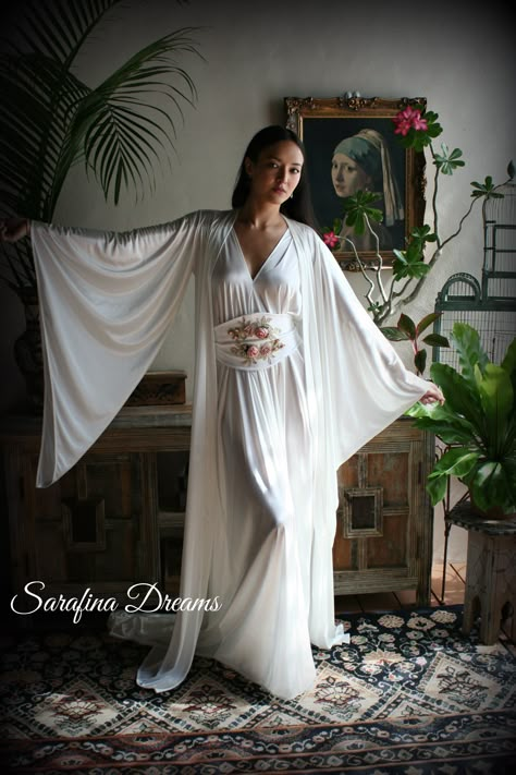 "White satin Bridal robe from our newest collection. Our satin is a stretch poly nylon that is the softest you'll find both inside and out so the fabric next to the skin is slinky and very silky. This is a match to our angel wing gown and is graced with long pointed wing sleeves. A classic kimono style that we've added a train to which adds a touch of glam and romance. Two side inseam pockets and it will come with a self fabric tie sash belt to close. It is shown with the angel wing gown which i Kimono Wedding Dress, Winged Sleeves, Wedding Sleepwear, Moda Kimono, Satin Bridal Robe, Vintage Loungewear, Night Gown Dress, Bridal Nightgown, Robe Wedding