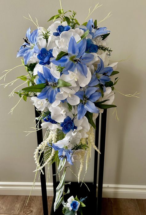 "🌹Large cascade bouquet and boutonniere with blue & white silk flowers/Bridal cascading bouquet with orchids and lilies/Wedding drop bouquet This wonderful large cascade bouquet is handmade with high quality artificial flowers such as: orchids, lilies, blue cherry flowers and greenery. The listing includes the cascading bouquet and groom boutonniere. Dimensions: 28\"-30\" long and approx. 15\"wide ( upper part). The stems are wrapped with satin ribbon. Bridesmaid bouquets and boutonnieres are available upon request. Please contact me. Matching arch arrangement you can find here: https://www.etsy.com/ca/listing/1221822062/2pcs-tropical-wedding-arch-flowerscorner?click_key=bd9ca0b9bd7445460908752f160c86507450aa22%3A1221822062&click_sum=ba1891da&ref=shop_home_active_49&sts=1 For more of my w Blue Flower Wedding Bouquet, Blue Lily Bouquet, Blue Lily Flower Bouquet, Blue Cascading Wedding Bouquets, Lilly Bouquet Wedding, Blue Stargazer Lily Bouquet, Stargazer Lilies Bouquet, Blue Hydrangea White Lily Bouquet, Blue And White Cascading Bridal Bouquet