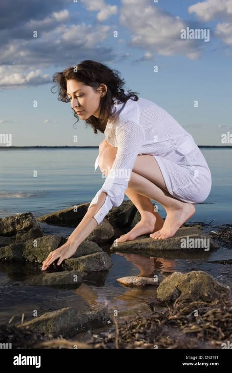 Download this stock image: Woman in white dress crouching on rocks by sea - CN319T from Alamy's library of millions of high resolution stock photos, illustrations and vectors. Woman In White Dress, Figure Studies, Body References, Woman In White, Stock Photos Woman, Sketches Of People, People Poses, Human Reference, Sitting Poses