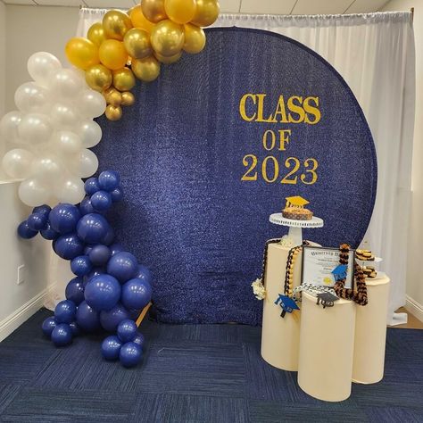 Throw an exciting Graduation party and create a splendid backdrop decor. Hang white curtains and set a round metal backdrop stand covered in a navy-blue shimmer spandex cover in front. Arrange a chic gold, white, & navy-blue balloon garland and stick gold glitter stickers spelling CLASS OF 2023 to add instant visual elegance. Arrange beige spandex covered cylinder pedestal stands exhibiting the party cake and other party related decorative accents and make your backdrop stand out. Blue Graduation Decorations, Metal Backdrop Stand, School Reunion Decorations, Metal Backdrop, Cylinder Pedestal, Gold Theme Party, Event Decor Ideas, High School Graduation Party Decorations, Party Decorations Table