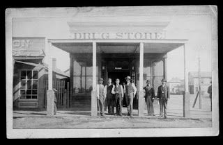 This photograph shows an exterior view of the Drug Store on the northwest corner of 2nd and Front Street in Dodge City, Kansas. Several men are seen posing for the photograph in front of the store, and a boy is partially visible behind the post on the left. The man on the right of the group is Dr. T. L. McCarty, identified as the first doctor in Dodge City.  Date: Between 1875 and 1885. Dodge City Kansas, Old West Town, Old West Photos, Kansas Usa, West Town, Dodge City, Western Town, American Frontier, Oregon Trail