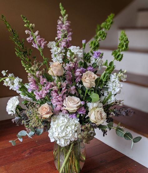 A lovely mix of spring blooms in tranquil shades of white, green, lavender and peach. This garden style bouquet may include: bells of Ireland, stock flower, snapdragons, carnations, hydrangea, roses, waxflower, and mixed greens. Upgrade to transform this design from "front-facing" to "360 degrees".   We use only the fr Purple White Green Flower Arrangements, Wide Flower Arrangements, Green And Purple Flower Arrangements, English Garden Flower Arrangements, Stock Flower Arrangements, Snapdragon Flower Arrangement, Jw Memorial Flowers Arrangements, Easter Bouquets Floral Arrangements, March Flower Arrangements