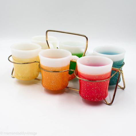 "Rainbow of Fire King Glamalite mugs in a cool mid-century modern brass carrier. These fun colors will brighten your day!   These mugs were manufactured by Anchor Hocking in the 1950s. Fire-King is an Anchor Hocking brand of glassware similar to Pyrex.  The mugs in this set have a colored vinyl/rubber coating with glitter and a wide white rim. They each have a different color: dark teal, apple green, light yellow, bright yellow, red, and orange. The original label (not available here) stated that these tumblers are \"Thermo Insulated/Keeps Drinks Hot or Cold Twice as Long/Needs No Coaster.\" Condition: The mugs are in very good condition with no cracks or chips. The teal mug, however, has a black stain visible in the last photo. The carrier is in fair condition with some wear.  Dimensions: Vintage Wishlist, Fire King Dishes, Rainbow Kitchen, Mid Century Glassware, Antique Shopping, Vintage Coffee Cups, White Rims, Vintage Kitchenware, Red And Orange