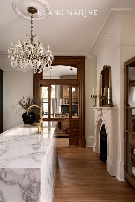 A kitchen showcasing a marbled countertop and a beautifully crafted fireplace mantel adorned with vintage décor. Adjacent to the kitchen is the butler's pantry, featuring wooden flooring, cabinets, doors with transoms. Parisian Style Kitchen, French Provincial Interior Design, Classic Modern Interior, Space Layout, Parisian Home Decor, Parisian Interior, European Style Homes, European Home Decor, French Country Kitchen