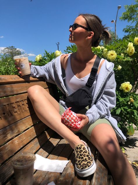 Girl sitting on bench with an ice chai tea latte in one hand and a sandwich in a wrapper in the other. Looking off to the side wearing a black lululemon Fanny pack across her chest, wearing green lululemon tight biker shorts, a white lululemon align tank top, and an oversized grey zip up sweater that is undone, with cheetah print vans slides Lululemon Fanny Pack Outfit, Black Fanny Pack Outfit, Green Biker Shorts Outfit, Crossbody Fanny Pack Outfit, Hip Pack Outfit, Fanny Pack Outfit Summer, Align Tank Outfit, Fanny Pack Outfit Street Styles, Fanny Pack Aesthetic