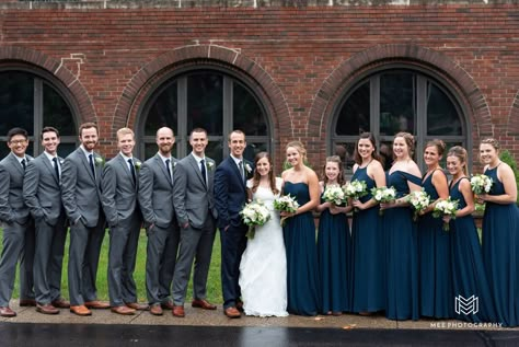 Groomsmen wearing gray suits and bridesmaids in navy dresses. Navy Blue Wedding Bridal Party, Navy And Grey Wedding Colors, Navy Bridesmaids And Grey Groomsmen, Navy And Gray Wedding Party, Navy Blue Bridesmaids And Groomsmen, Navy Groomsmen Suits And Bridesmaids, Navy Bridesmaids And Groomsmen, Dark Grey Groomsmen Suits, Navy Blue And Grey Wedding