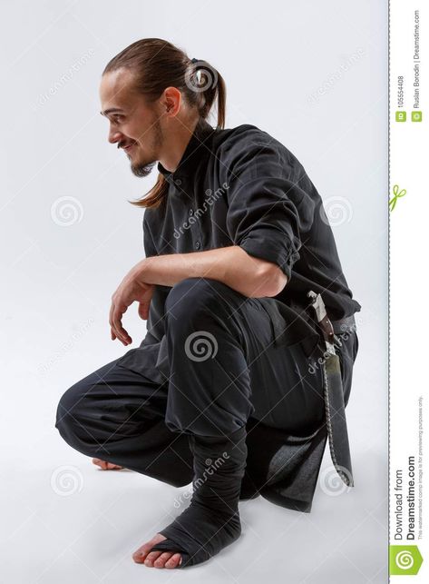 Photo about Ninja young with a beard in black uniform and a grin sat on one knee close-up on a gray background. Image of caucasian, background, dark - 105554408 Guy Kneeling Pose, Sitting Knees Up Reference, Guy Kneeling, Down On One Knee, Black Uniform, Background Dark, Knee Up, Sitting Poses, Person Sitting