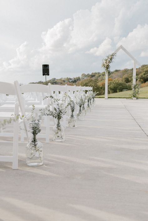 Ceremony floral installation on white arbor with textural white and neutral flowers and greenery. Clear glass jugs with greenery lining the ceremony aisle Flower Vases Down Aisle, Glass Jugs Wedding Aisle, Wedding Isles Decoration Chapel, Carboys Wedding, Eucalyptus Wedding Ceremony Aisle, Isle Ceremony Decorations, Classic Ceremony Decor, Wedding Aisle Flower Vases, Glass Jug Wedding Aisle