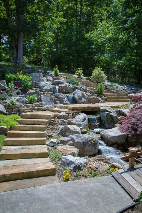 Modern Design Aquascaping did a tear-out & re-installation of a pondless waterfall in Lenoir City, TN. The feature which was done by Modern Design Aquascaping, includes large mountain boulders,cedar driftwood accents, LED under-water lighting, flagstone walkway-steps-and bridge, and a wooden bridge. Cascade Waterfall Garden, Backyard Creek Landscaping, Mountain Garden Ideas, Pondless Waterfall, Flagstone Walkway, Fountains Backyard, Sloped Backyard, Pond Landscaping, Backyard Water Feature