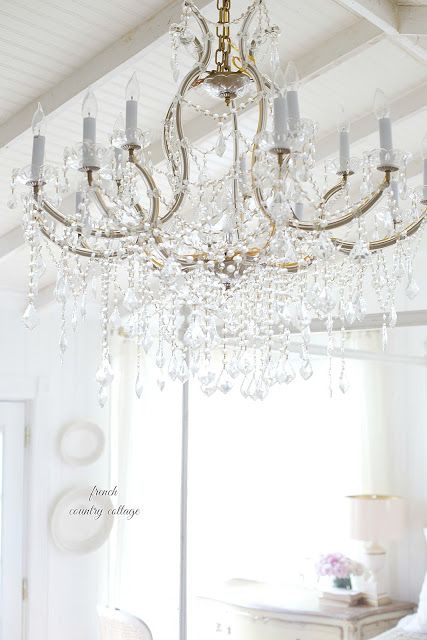 A large crystal chandelier hangs over a white themed room. Shabby Dresser, Kitchen Chandelier Over Table, Bling Chandelier, Chandelier Over Table, Cottage Kitchen Inspiration, French Country Chandelier, Country Chandelier, French Vintage Decor, Kitchen Chandelier