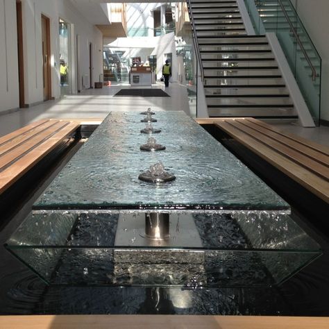 A stunning water feature. The design has multiple concentric rings of water that are brought to life with the light through the glass.  Water falling like rain around the outside gives another dimension as well as sound. Luxury Water Feature, Residential Water Feature, Indoor Water Features Living Rooms, Lobby Water Feature, Lobby Reception Design, Indoor Waterfall Wall, Garden Water Features, Reception Area Design, Indoor Water Features