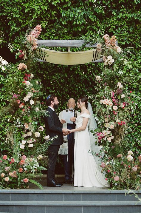 Bride and Groom hold hands under a gorgeous summer garden chuppah at Four Seasons Beverly Hills. Their Rabbi is draped with a Talit as he reads from his script. Green Chuppah, Wildflower Aisle, Chuppah Wedding, Purple Napkins, Candles Purple, Chuppah Ideas, Aisle Arrangements, Jewish Wedding Ceremony, Wedding Corset