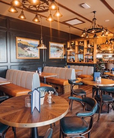 Pub interior with booths, padded seating and round tables. Coastal Pub Interior, New England Restaurant Design, Oyster Restaurant Design, Lake Restaurant Design, Cozy Restaurant Aesthetic, Country Pub Interior, Nantucket Restaurants, German Interior Design, Coastal Restaurant