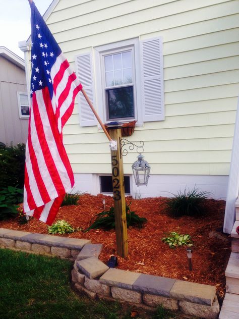 Memorial Day project. Address display post.4x4 deck post, solar cap light, flag mount, and lantern/flower hanger Flag Hanging Ideas Outside, Flag Poles Ideas, Flag Post Ideas, Wrap Around Post Planter, Outdoor Flag Display Ideas, Flag Poles In Front Yard, Flag Pole Planter, Landscape Around Flag Pole, American Flag Pole Landscaping