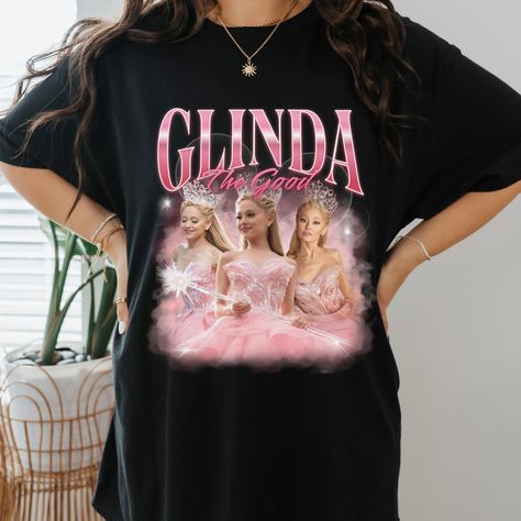 "Vintage 90s bootleg t-shirt featuring Ariana Grande as Glinda from Wicked. This unique design showcases a whimsical illustration of Glinda with vibrant colors and playful text, perfect for musical theater fans and collectors. Ideal for casual wear or as a standout piece in any wardrobe. Shop now for a touch of Broadway nostalgia! Glinda Popular, Wicked Ariana Grande, Ariana Grande Vintage, Wicked Merch, Glinda Wicked, Wicked Glinda, Glinda The Good, Merch Shirt, Glinda The Good Witch