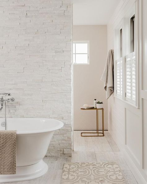 Custom bathroom design featuring a white staggered stone wall behind a roll-top bathtub paired with a wall mount tub filler. White Stone Bathroom Ideas, Shower Behind Bathtub, Tile Wall Behind Tub, Shower Behind Wall, Wall Behind Bathtub, Bathroom With Stone Wall, Stone Wall Bathroom, Shower Behind Tub, White Stone Bathroom