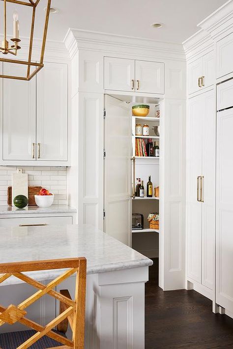 A white hidden pantry door fixed beneath white kitchen cabinets is fitted with a long brass handle and opens to a pantry boasting stacked white shelves. Hidden Pantry Door, Shiplap Trim, Pull Out Kitchen Cabinet, Slab Backsplash, Kitchen Pantry Doors, Hidden Pantry, White Island, Built In Pantry, Pantry Shelves