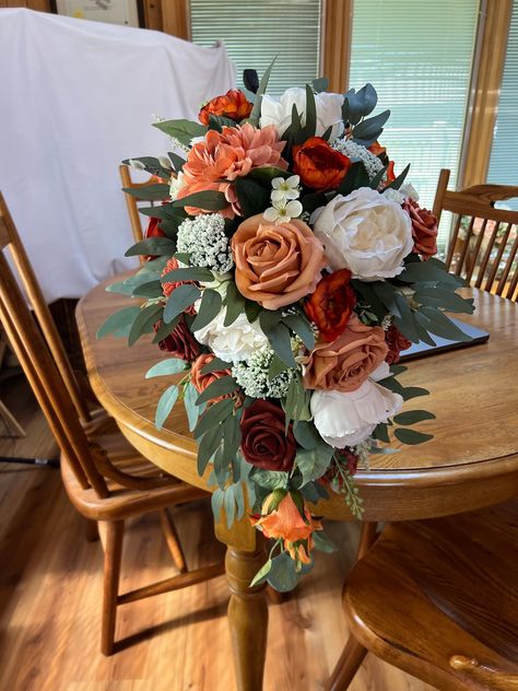 This is a fall cascade of terracotta, cream, burnt orange, and peach with sage colored greenery. Inspired by The color collection Terracotta Sunset this bouquet will be beautiful for your fall wedding.  It is made on a traditional bouquet holder that can be wrapped in ribbon or burlap to conceal.  It is 22 inches long. Also pictured are large round bridesmaids bouquets. I can created pieces for your entire wedding party if you choose. Terracotta Cascading Bouquet, Champagne And Terracotta Wedding Theme, Fall Cascade Wedding Bouquet, Wedding Bouquets With Roses, Terracotta Flower Bouquet, Spice Wedding Colors, Terracotta Wedding Ideas, Burnt Orange Flower Arrangements, Faux Flower Arrangements Wedding