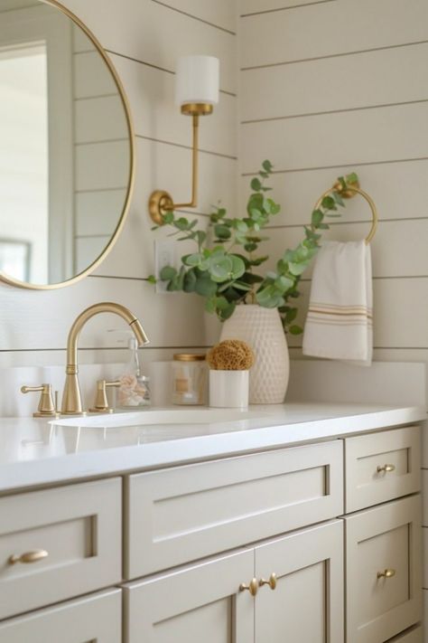 Bathroom sink with gold fixtures, clean countertop, round mirror, wall lamp, eucalyptus in a vase, and a hand towel. Good Fixtures Bathroom, Hall Bath Decor, Neutral Home Inspiration, Bathroom Design Ideas 2024, Beige Bathroom Vanity Cabinets, Beige Bathroom Color Schemes, Neutral And Gold Bathroom, Light Colored Bathrooms, Small Bathroom Neutral Colors