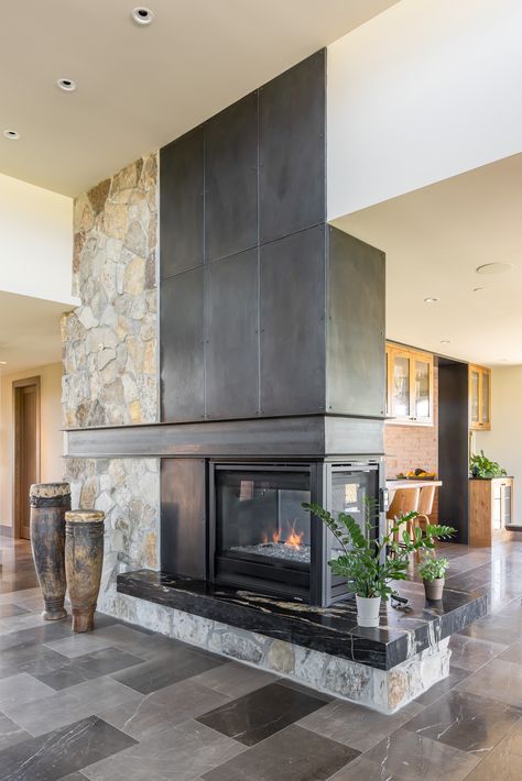 Steel + Stone double sided fireplace. Large African drums, plants, tile floor Double Sided Fireplace Kitchen Living Room, Mid Century Modern Double Sided Fireplace, Double Sided Fireplace Between Kitchen And Living Room, Double Sided Chimney, Four Sided Fireplace, Stone Fireplace Halfway Up Wall, Double Sided Fireplaces, 4 Sided Fireplace, Double Sided Fireplace Bedroom