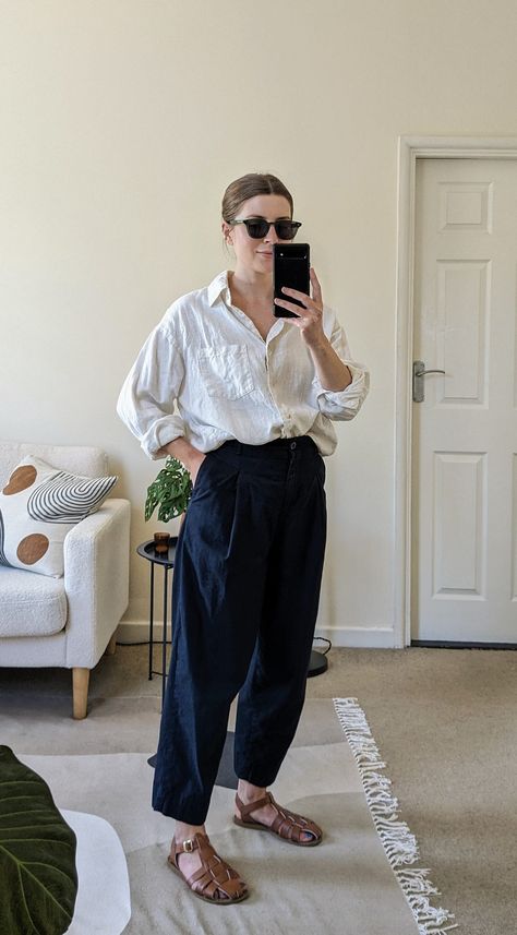 A woman stands in front of a mirror. She wears green sunglasses, a white linen shirt open at the collar, cropped navy trousers and brown fisherman sandals. Cropped Linen Trousers Outfit, Walking On The Beach Outfit, Classic Preppy Summer Outfits, Mom Fashion Casual, Navy Sandals Outfit, Fisherman Beanie Women Outfit, Cool Minimalist Outfits, Outfit With Linen Shirt, Styling Linen Trousers