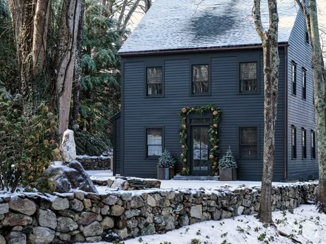 The exterior of the home is painted Benjamin Moore’s Deep River. At holiday time, galvanized steel planters from Design Within Reach are filled with miniature blue spruces. #housegoals #houseexteriors #homeinspo Dark Colonial Exterior, Blue House Dark Trim Exterior, Deep Blue House Exterior, Dark Navy Blue Exterior House, Blue House Dark Trim, Navy Blue House With Black Trim, Dark Trim House Exterior, Moody Blue House Exterior, Dark Blue House Exterior Navy Color Palettes