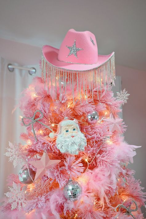 For a disco cowgirl Christmas decor theme, start with a color palette of light pink and silver. From there, incorporate motifs like disco balls, cowgirl boots and hats, horses and horseshoes, classic star shapes, and rhinestones and pink feather boas. Disco ball string lights is another way to channel the theme. I’d also recommend creating focal points throughout your space to highlight the theme such as hanging disco balls from the ceiling or DIYing a rhinestone cowgirl hat tree topper. #Boho_Pink_Christmas_Tree #Pink_Disco_Christmas_Tree #Disco_Cowgirl_Christmas_Tree #Pink_Tree_Topper Disco Ball Tree Christmas, Pink Western Decor, Christmas Tree Mesh Ribbon, Disco Ball String Lights, Hanging Disco Balls, Rhinestone Cowgirl Hat, Western Collage, Disco Christmas, Cowgirl Christmas