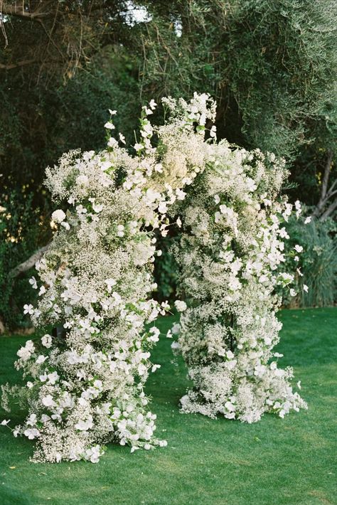 With all the foliage around the lawn, we wanted to create a focal point with the wedding arch using color—in this case, white—and lots of texture. Dogwood and baby’s breath were the perfect florals and created a wow factor for the ceremony space. We designed a ‘planted garden’ of all-white arrangements which dotted the ceremony aisle in clusters. As the sun set, it was breathtaking to see the contrast of the white against the green.” White Flower Arch, White Floral Arch, The Parker Palm Springs, Parker Palm Springs, Ceremony Design, Wedding Ceremony Flowers, Ceremony Inspiration, White Wedding Flowers, Ceremony Arch