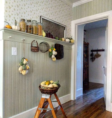 The lovely combination of beadboard and wallpaper is the ideal pairing to decorate a country kitchen. Pegs protrude from a floating shelf that acts as trim for the wainscoting and provides an additional place to store and display kitchen dÃ©cor. A small wooden step stool hosts a basket of gourds, which are also displayed along the shelf above. Wallpaper And Wainscoting, Beadboard And Wallpaper, Kitchen Beadboard, Beadboard Wall, Beadboard Kitchen, Dining Room Decor Rustic, Wainscoting Kitchen, White Beadboard, Beadboard Wainscoting