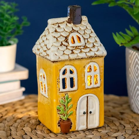 Village Pottery Yellow Garden House Tealight Holder    This gorgeous ceramic tealight holder is the perfect way to create a cosy ambience in your own home.   The charming ceramic house features a rustic design with a potted plant out the front and a tiled roof. Decorated with a cream and yellow glaze, this charming tealight holder will look lovely when displayed on a shelf or windowsill. Place a tealight of your choice inside the rear of the house and watch the glow from the flame light up behind the windows of the house.   Not just for tealights, this unique piece doubles as a decorative ornament. Combine with more pieces from the Village Pottery range to build your own little decorative village on your coffee table, shelf or windowsill. It makes the perfect birthday, Mother’s Day, or Chr Ceramics Plant Pot, Ceramic House Ornaments, Ceramic Tealight Holder, Ceramic Houses Pottery, Ceramic Cottage House, Clay House Candle Holder, Ceramic Tea Light Houses, Tealight House, Ceramic House Tea Light Holder