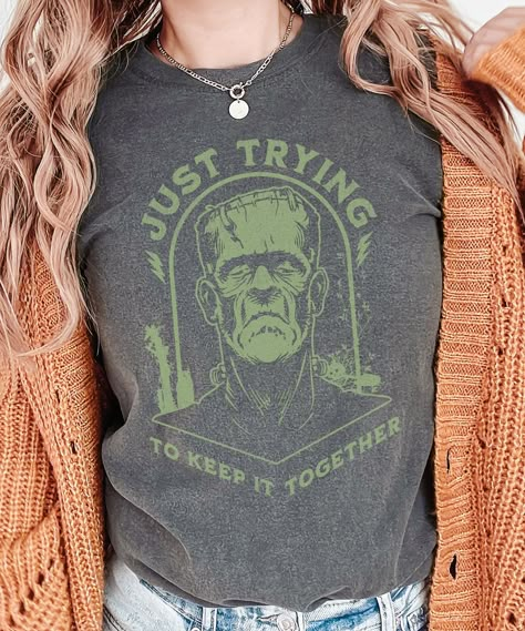 Get ready to keep it spooky and stylish this Halloween with our exclusive 'Just Trying to Keep It Together' Frankenstein Halloween shirt! Perfect for those who love a little Halloween humor, this unique shirt features a distressed Frankenstein design with the quote 'Just Trying to Keep It Together' adorned across the front. Made from soft, high-quality fabric, this shirt offers both comfort and style. Wear it to Halloween parties, trick-or-treating, or simply to celebrate the spirit of the season. Grab yours now and show off your love for Halloween in a fun and fashionable way! Graphic is distressed for a vintage look. Please check the size chart and size up a couple sizes for an oversized look. *The larger the shirt, the larger the graphic.  Our printer sizes the graphics proportionate to Cricut Halloween Shirt Ideas, Vinyl Halloween Shirts, Cricut Halloween Shirt, Fall Shirt Designs, Halloween Tshirt Ideas, Frankenstein Design, Trying To Keep It Together, Halloween Inspired Outfits, Halloween Shirt Ideas