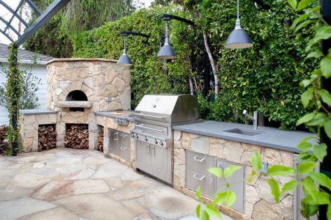 This stunning state-of-the-art outdoor kitchen features stone cabinets adjacent to a gorgeous wood-burning oven. Lush greenery and hanging ivy provide a phenomenal natural backdrop. Outdoor Kitchen Stone, Hot Tub Pergola, Outdoor Sink, Kitchen Stone, Curved Pergola, Natural Tile, Wood Burning Oven, Natural Fence, Living Fence