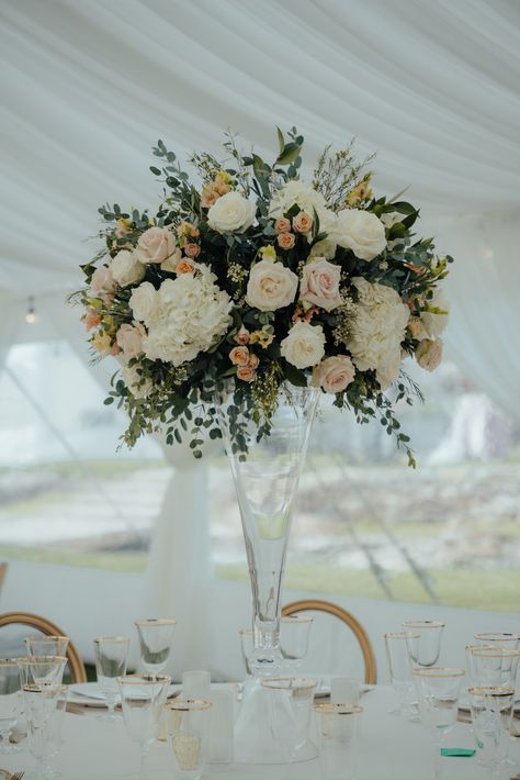 Singular tall, round flower arrangement featuring blush and ivory flowers. Hydrangea roses, miniature roses, lisianthus,  and greenery. the table setting is clear glass with gold accents. Blush Pink Tall Wedding Centerpieces, Wedding Centerpieces Flowers Tall, Glass Trumpet Vase Centerpiece, Tall Flower Arrangements Wedding, Tall Wedding Centerpieces Elegant, Wedding Flowers Centerpieces, Trumpet Vase Centerpiece, Tall Flower Vase, Modern Wedding Centerpieces