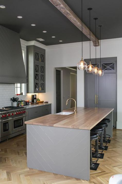 Gray kitchen features four glass pendants illuminating a gray herringbone center island topped with honey stained wood countertops fitted with a sink and brass gooseneck faucet lined with backless industrial bar stools placed atop a light wood herringbone wood floor. Dark Ceiling Light Walls, Rustic Kitchen Ideas, Herringbone Kitchen, Contemporary Style Kitchen, Dark Ceiling, Off White Kitchens, Grey Wood Floors, Herringbone Wood Floor, Wood Floor Kitchen