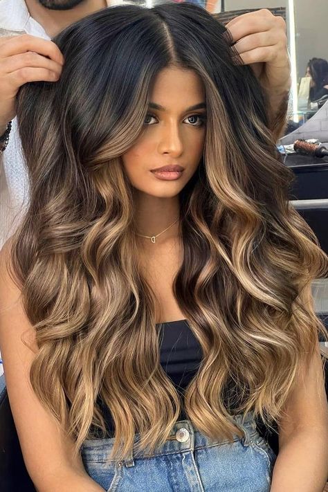 Long voluminous waves with a center part, blending black hair with rich caramel balayage. The cascading curls add depth and movement, enhancing the multi-tonal effect for a glamorous look.  // Photo Credit: Instagram @solotreartofbeauty Caramel Balayage For Black Hair, Caramel Hair Balayage Honey, Caramel Balayage Dark Roots, Dark Brown Hair With Caramel And Blonde Highlights, Dark Long Hair Balayage, Light Caramel Highlights On Black Hair, Baliage Hair Fall, Black With Caramel Balayage, Caramel Blonde Balayage On Black Hair