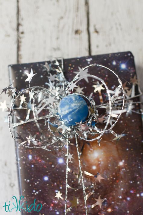 DIY space gift wrapping paper (so easy!) and a celestial bow made out of star garland and a bouncy ball.  Simple, fast, and perfect for any fan of space or science fiction! Space Gift Wrapping Ideas, Birthday Wrapping Ideas, Galaxy Crafts, Space Gifts, Gift Wrapping Tutorial, Pony Gift, Wrapping Tutorial, Celestial Theme, Solstice Celebration